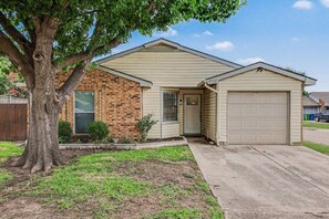 A residential house with a brick facade, a front door, and a garage. - Cozy Colony Cottage (The Colony)