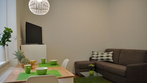 A modern living room with a brown sofa, a dining table with green placemats, a pineapple, and a TV mounted on the wall. - Studio Apartments City&style (Zagreb)