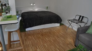 A modern bedroom with a bed, a desk with a chair, a small table with a bowl and a jar, and a green plant. - Studio Apartments City&style (Zagreb)