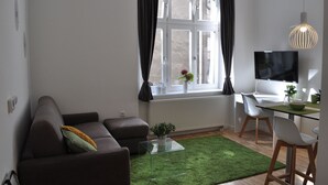A modern living room with a sofa, a glass coffee table, a desk with a computer, and a large window with curtains. - Studio Apartments City&style (Zagreb)