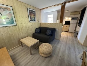 A cozy room with a wooden wall, a dark sofa, a small wooden table, and a woven pouf. - BOIS FLOTTE - VIELLE SAINT GIRONS (VIELLE SAINT GIRONS)