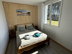 A bedroom with a wooden headboard, a bed with a white and blue bedspread, two pillows, a window with a view of trees, and a painting on the wall. - BOIS FLOTTE - VIELLE SAINT GIRONS (VIELLE SAINT GIRONS)