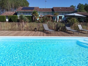 A swimming pool with lounge chairs, a wooden deck, and a building with a tiled roof in the background. - BOIS FLOTTE - VIELLE SAINT GIRONS (VIELLE SAINT GIRONS)