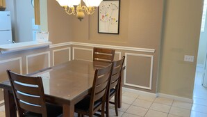A dining room with a large table, four chairs, a chandelier, and a framed picture on the wall. - Spacious 3-bedroom apartment, in the best community from Disney. (Kissimmee)