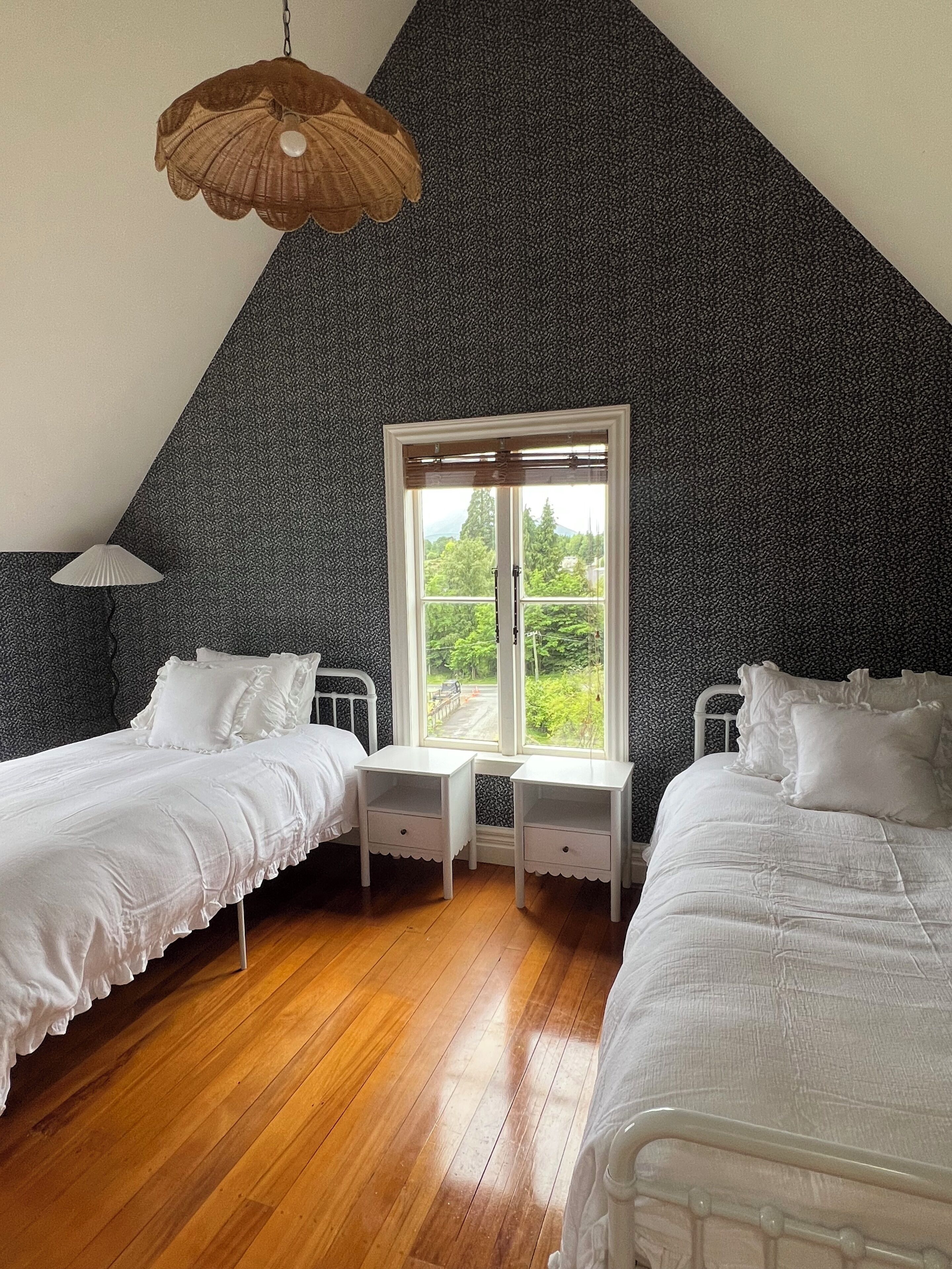 A bedroom with two beds, a window, and a hanging lamp.