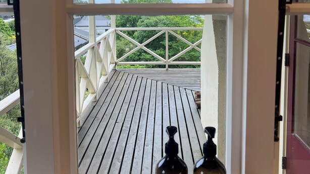 Een houten terras met uitzicht op bergen en een meer. Er staan twee flessen op het terras.