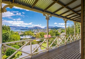 A covered balcony with a view of a town, mountains, and a lake.