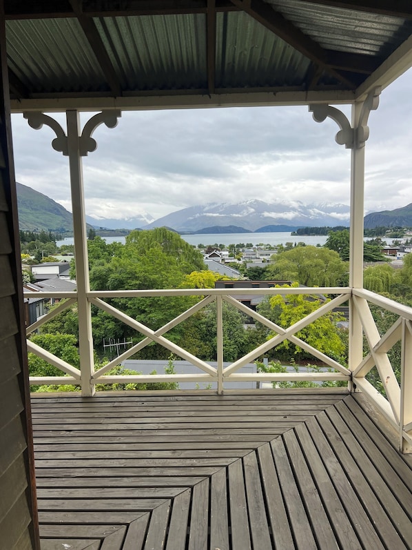 Une terrasse en bois dotée d’une rambarde, offrant une vue sur un paysage montagneux et une étendue d’eau.