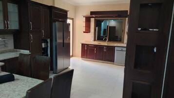 A kitchen with dark wooden cabinets, a stainless steel refrigerator, a built-in oven, and a window above the sink.