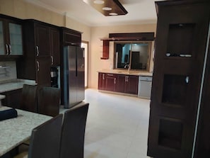 A kitchen with dark wooden cabinets, a stainless steel refrigerator, a built-in oven, and a window above the sink.