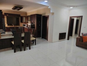 A modern kitchen with dark wooden cabinets, a dining area with a table and chairs, and a living room with a sofa.