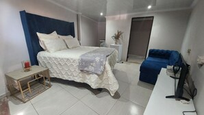 Quarto com cama, mesa de cabeceira, cadeira e uma pequena mesa com uma vela.