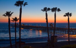 A pier extending into the ocean with palm trees and a lifeguard station.