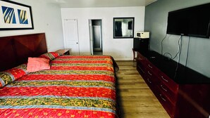 Quarto com cama, cômoda, televisão, porta e espelho.