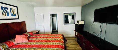 A bedroom with a bed, a dresser, a television, a door, and a mirror.