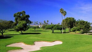 Campo de golfe com bunkers de areia, árvores e um céu azul límpido.