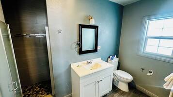 A bathroom with a shower, toilet, sink, and a window.