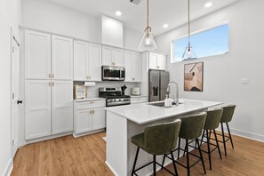 Una cocina moderna con armarios blancos, una isla central con taburetes de bar, electrodomésticos de acero inoxidable e iluminación colgante.