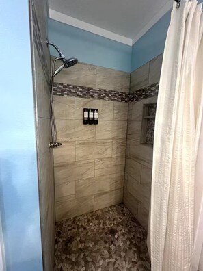 A shower with a tiled floor, a showerhead, and a curtain. - Stay Salty Cottage (Foley)