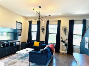 Ein modernes Wohnzimmer mit Fernseher, einem blauen Sofa, einem Couchtisch und einem Essbereich.