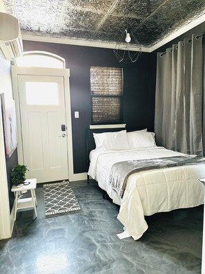 Ein Schlafzimmer mit einem Bett, einem kleinen Tisch mit Pflanze, einem gemusterten Teppich und einer Decke mit aufwendigen Verzierungen.