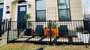 Un edificio de ladrillo de dos pisos con ventanas grandes, una puerta principal y un pequeño porche con plantas en macetas.
