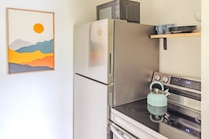 Een keuken met een koelkast, magnetron, waterkoker en oven.