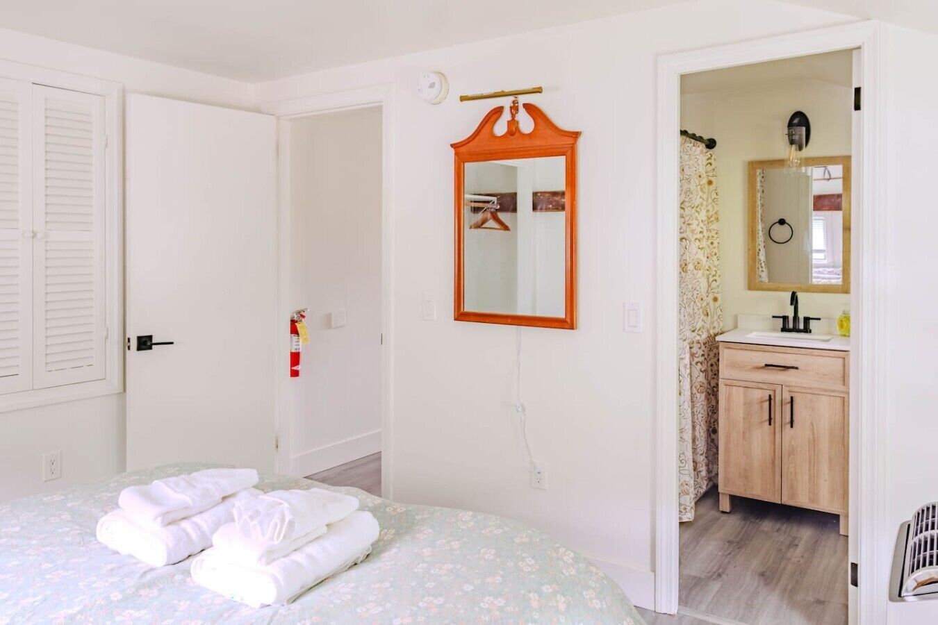 A bedroom with a bed, a bathroom with a sink and mirror, and a door leading to another room.