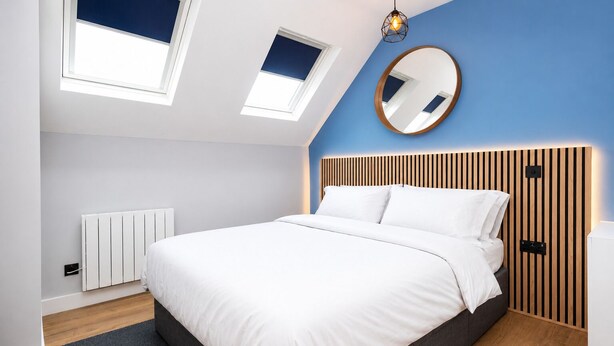 Een moderne slaapkamer met een bed, dakramen, een ronde spiegel en een houten hoofdbord.