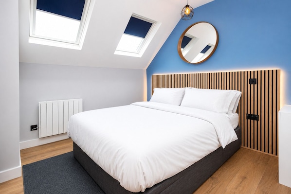 A modern bedroom with a bed, skylights, a round mirror, and a wooden headboard.