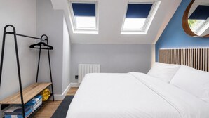 Een slaapkamer met een bed, dakramen, een radiator, een houten plank en een hangroede.