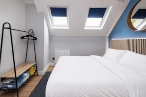 A bedroom with a bed, skylights, a radiator, a wooden shelf, and a hanging rack.