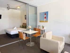 Ein Hotelzimmer mit einem Bett, einem Esstisch mit Stühlen, einer Couch, einem Deckenventilator, einem Gemälde eines Leuchtturms und einem großen Spiegel.