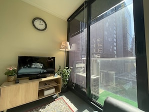 Ein Wohnzimmer mit Fernseher, einer Uhr, einer Lampe, einer Pflanze und einer Glastür zu einem Balkon.