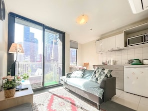 Eine moderne Wohnung mit Sofa, Esstisch, Küchenzeile und einer Glastür zum Balkon.