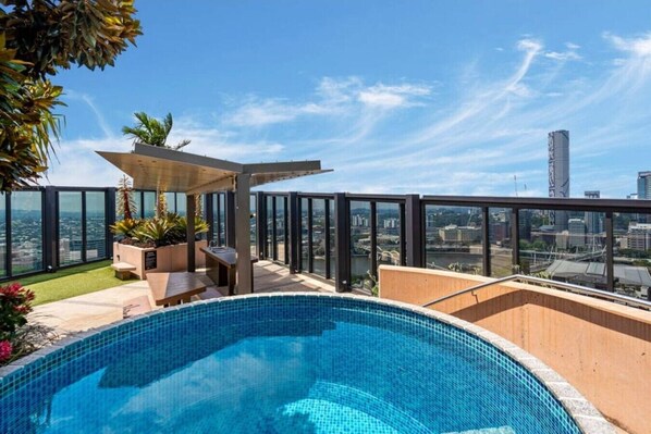 Ein Pool auf dem Dach mit Blick auf die Stadt, Sitzgelegenheiten im Freien und einer Pergola.
