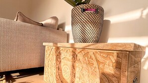 Ein Zimmer mit einer Couch, einem gewebten Blumentopf und einem geschnitzten Holznachttisch.