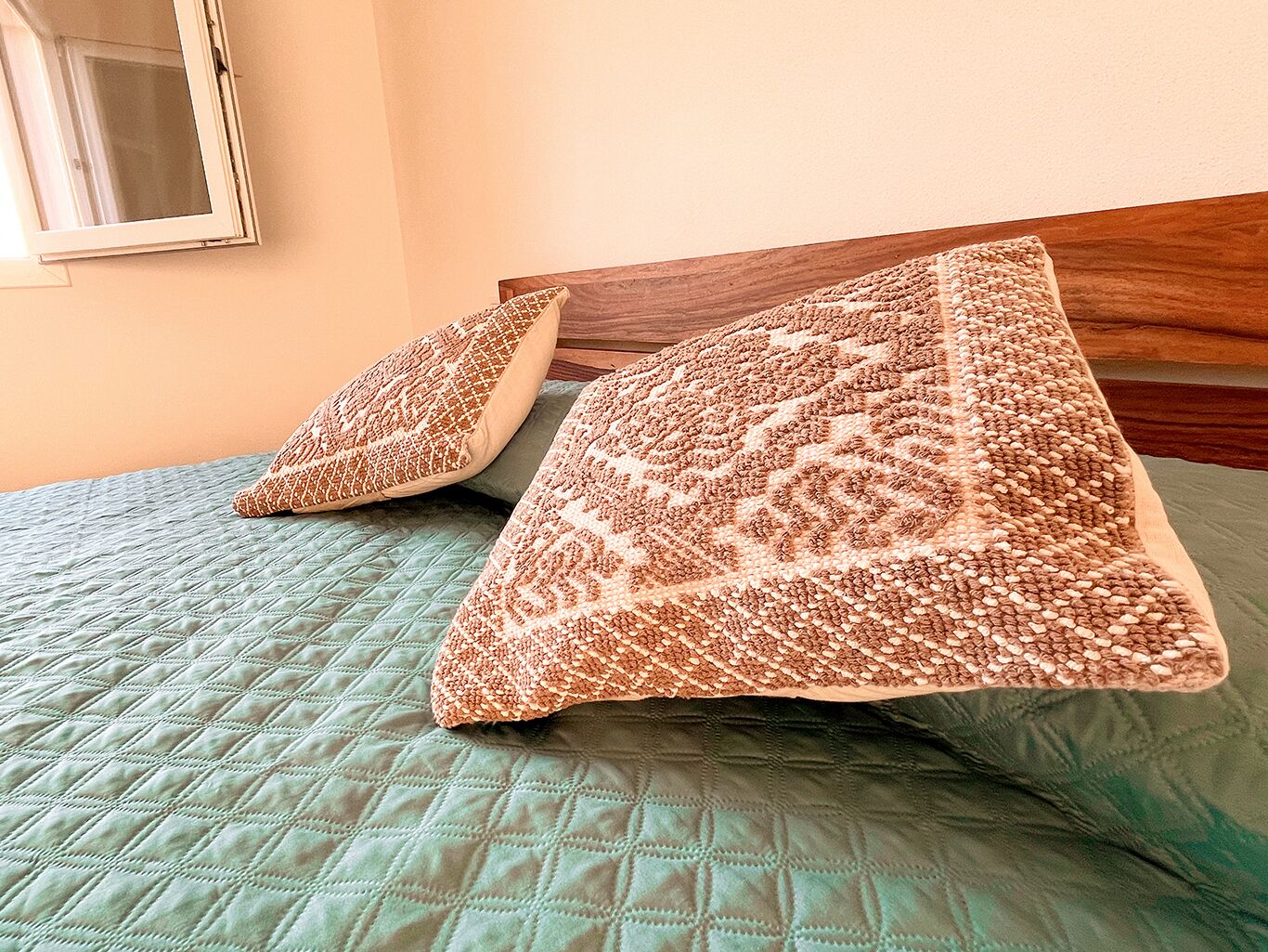 Un lit avec une couette verte et deux oreillers à motifs texturés.