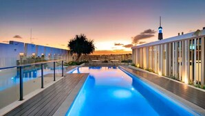 A swimming pool with a wooden deck, a palm tree, and a building with vertical windows. - Prime Spot: Modern 2BD/2BA with Pool & Parking M1 (South Brisbane)
