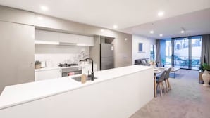 A modern kitchen with a central island, a dining area with a table and chairs, and a large window with a view. - Prime Spot: Modern 2BD/2BA with Pool & Parking M1 (South Brisbane)