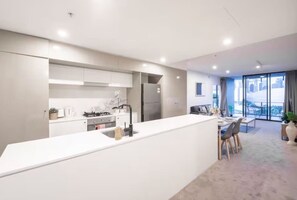 A modern kitchen with a central island, a dining area with a table and chairs, and a large window with a view. - Prime Spot: Modern 2BD/2BA with Pool & Parking M1 (South Brisbane)