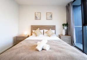 A hotel room with a large bed, two bedside tables, a nightstand, a window with curtains, and two wall-mounted artworks. - Prime Spot: Modern 2BD/2BA with Pool & Parking M1 (South Brisbane)