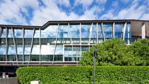 A modern building with a glass facade, a green hedge in the foreground, and a clear blue sky. - Prime Spot: Modern 2BD/2BA with Pool & Parking M1 (South Brisbane)
