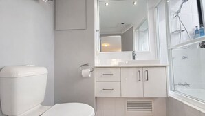Een moderne badkamer met toilet, wastafel, spiegel en douche.