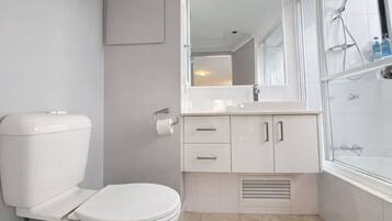 A modern bathroom with a toilet, sink, mirror, and shower.