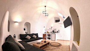 A compact living space with a sofa, coffee table, and a kitchen area with a TV. - The Petra Villa | Premium getaway blending modern luxury, authentic island charm (Thira)