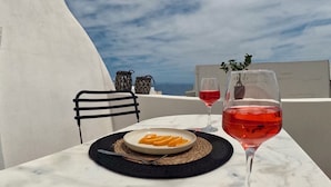 A table with a plate of food and a glass of red wine, set against a white wall with a view of the sky. - The Petra Villa | Premium getaway blending modern luxury, authentic island charm (Thira)