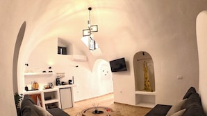 A cozy living room with a sofa, a coffee table, and a modern kitchen in the background. - The Petra Villa | Premium getaway blending modern luxury, authentic island charm (Thira)