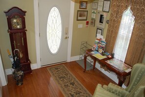 A room with a wooden floor, a door with a stained glass window, a grandfather clock, a desk with papers and a lamp, and a green armchair. - Private Room, Walk to Niagara Falls & Clifton Hill + Free Parking (Niagara Falls)