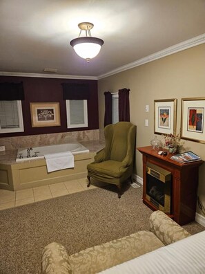 A room with a bathtub, a green armchair, a wooden cabinet with a fireplace, and framed artwork on the wall. - Private Room, Walk to Niagara Falls & Clifton Hill + Free Parking (Niagara Falls)
